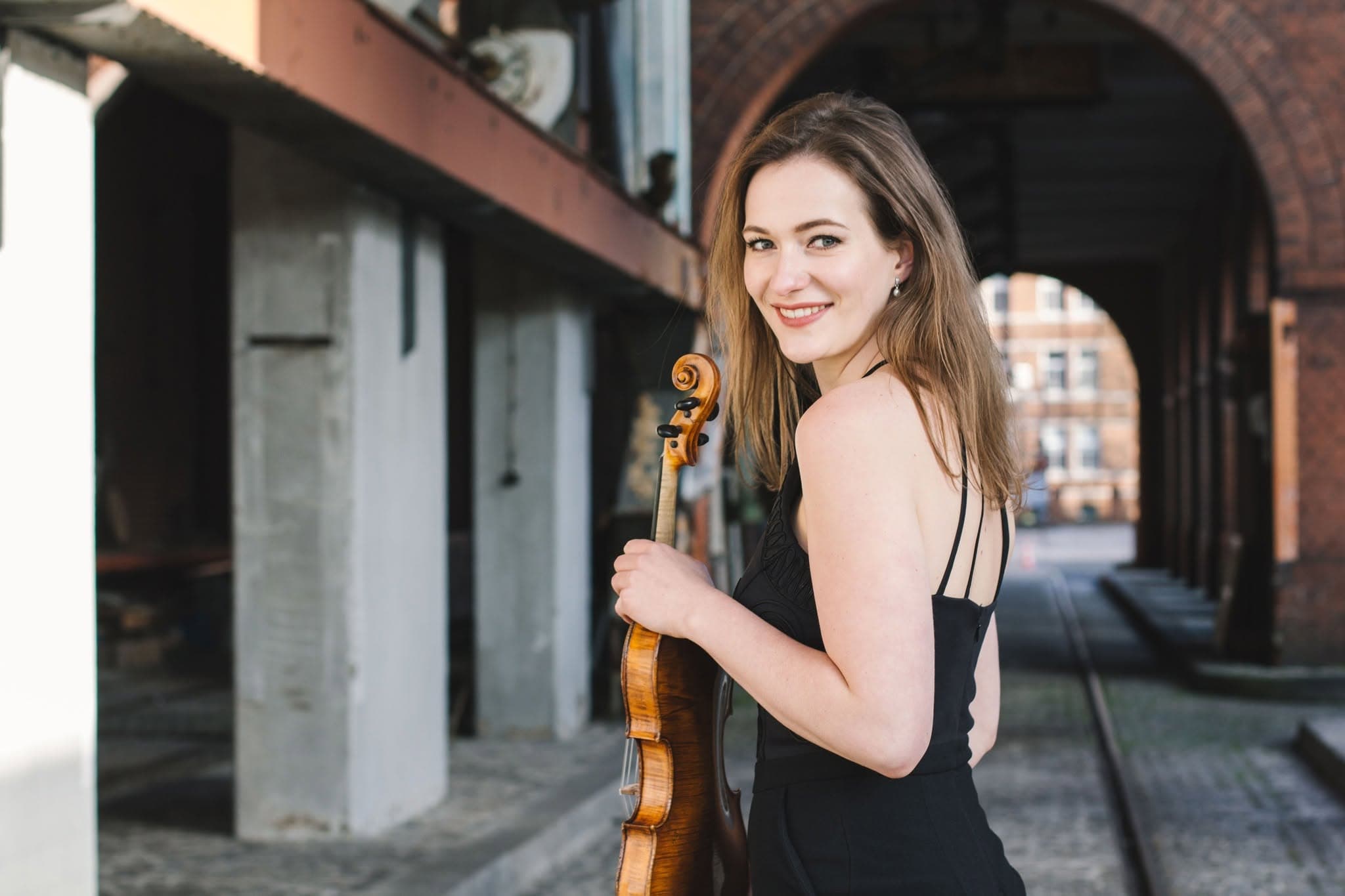 Violinist Larissa Cidlinsky smiling with her instrument under an archway